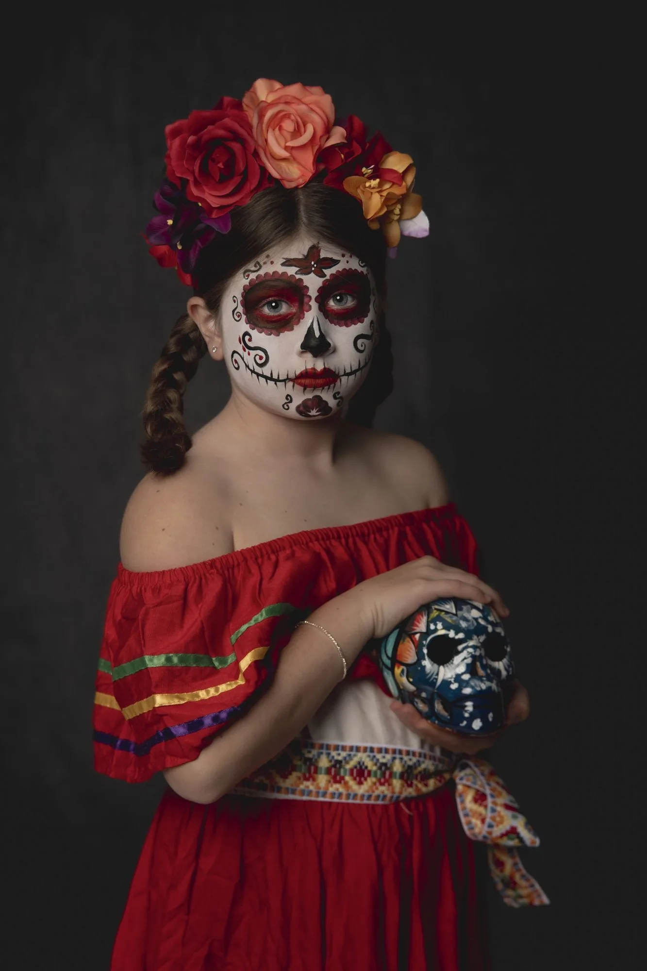 Girl in red sugar skull makeup and a rose crown holding a painted skull, Halloween costume portrait by Katie McBride Photography